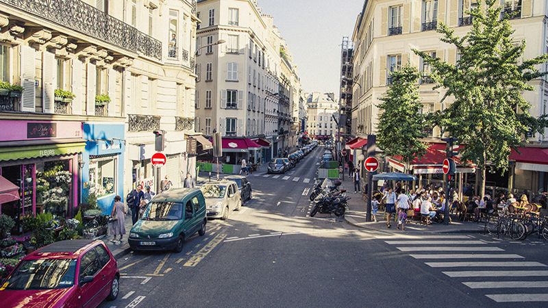 Street scene around the Opera district, which is in Paris 9th Arrondissement. Apartment buildings, stores, restaurants, cars and people are visible in the image.