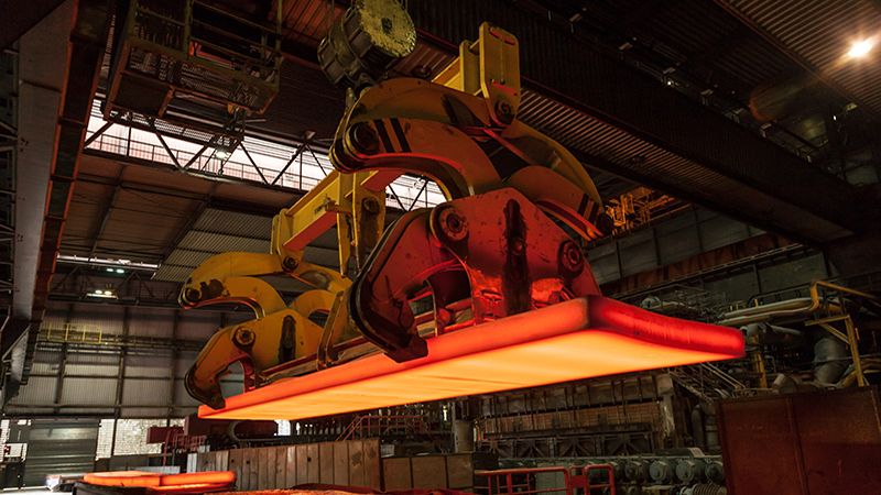 A glowing steel slab is loaded in the steelworks